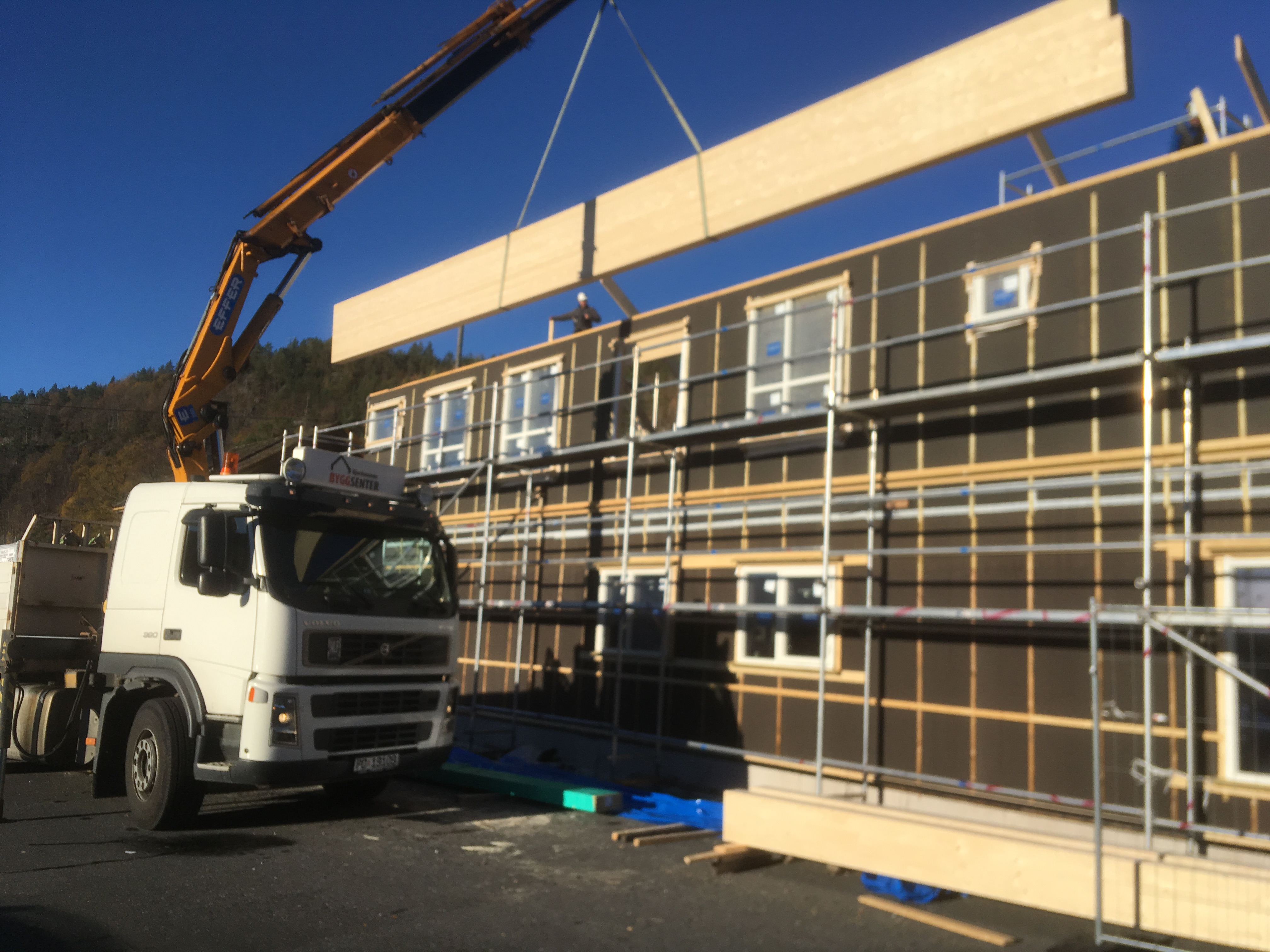 Lastebil med kran løfter takstoler på byggeplass